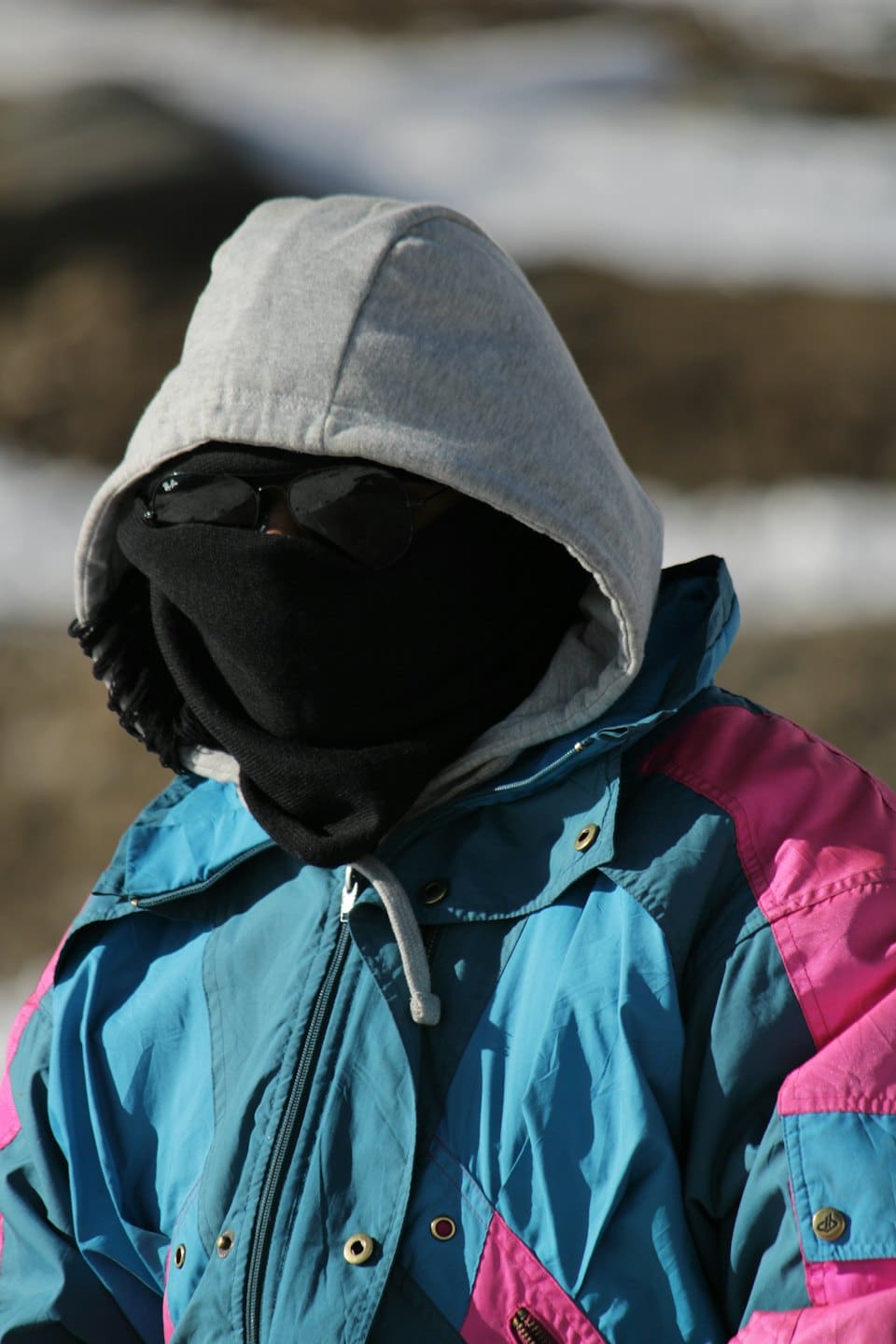 Person in a colourful ski jacket and balaclava outdoors.